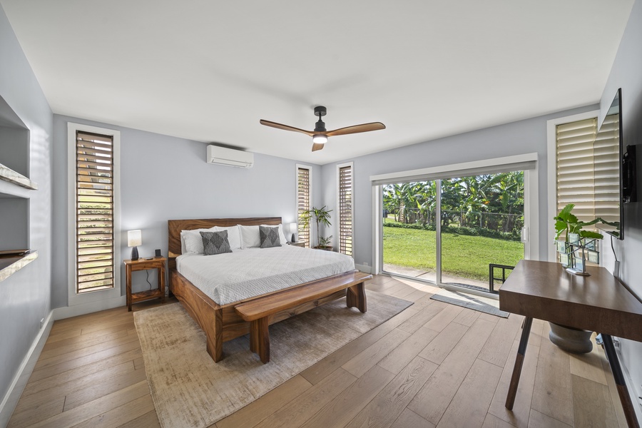 Primary bedroom featuring a king-sized bed, study desk, and a smart TV, with sliding doors to outdoor greenery.