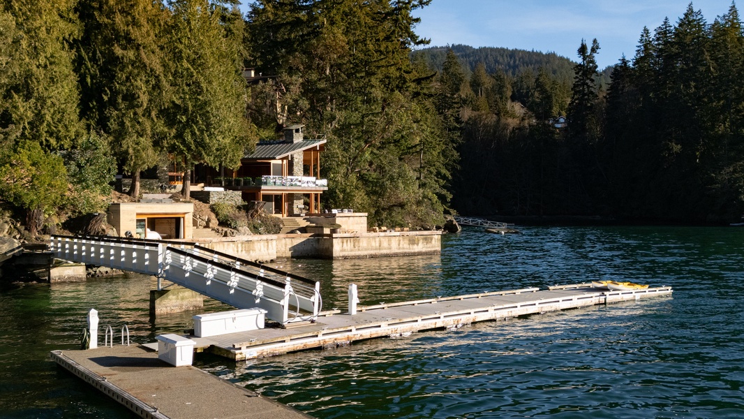 Stunning lakefront property with private dock nestled among towering evergreens and forested mountains.