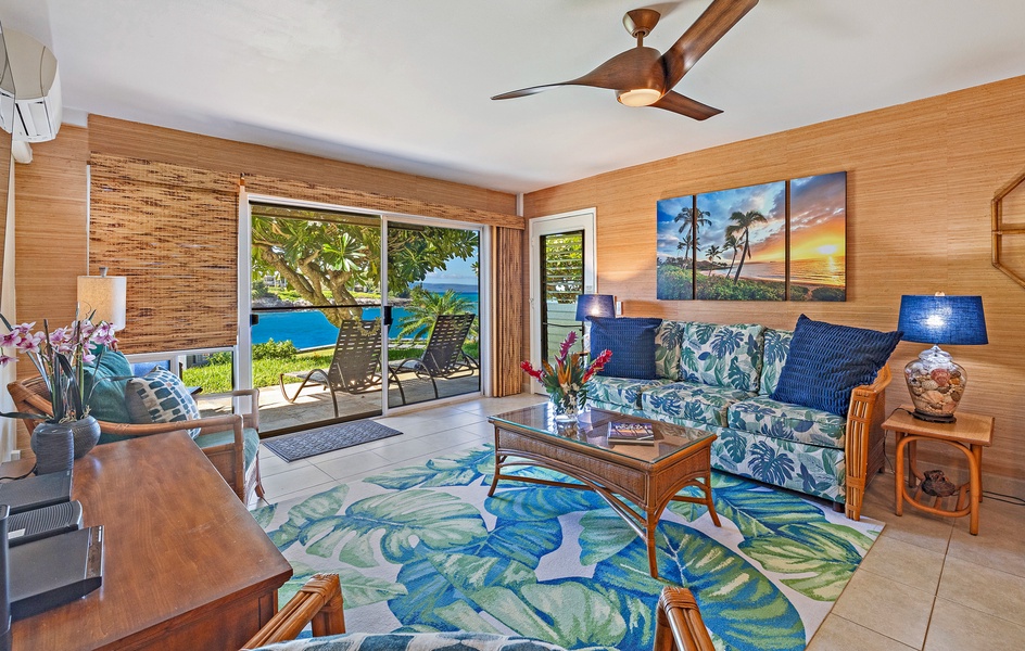 The living room features tropical décor with comfortable seating and direct access to a lanai with stunning ocean views, creating the perfect space for relaxation.