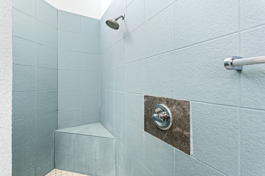 Cool-toned shower with a corner bench, offering a peaceful and practical rinse-off after time in the pool or hot tub.