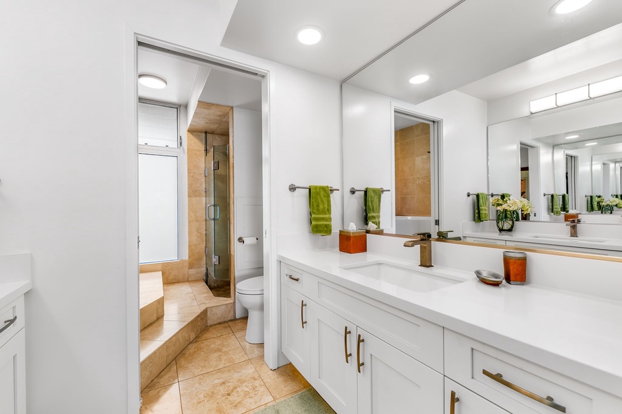 Crisp white cabinetry and backlit mirrors create a clean, modern bath experience, ideal for relaxing after beach days.
