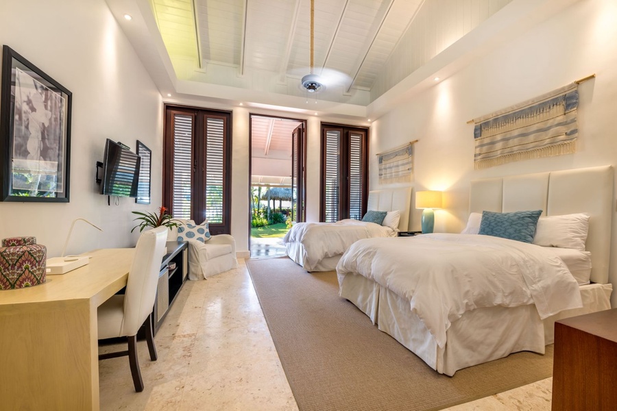 Guest bedroom with two plush beds, featuring soft padded headboards, a writing desk, and a cozy armchair by the window.