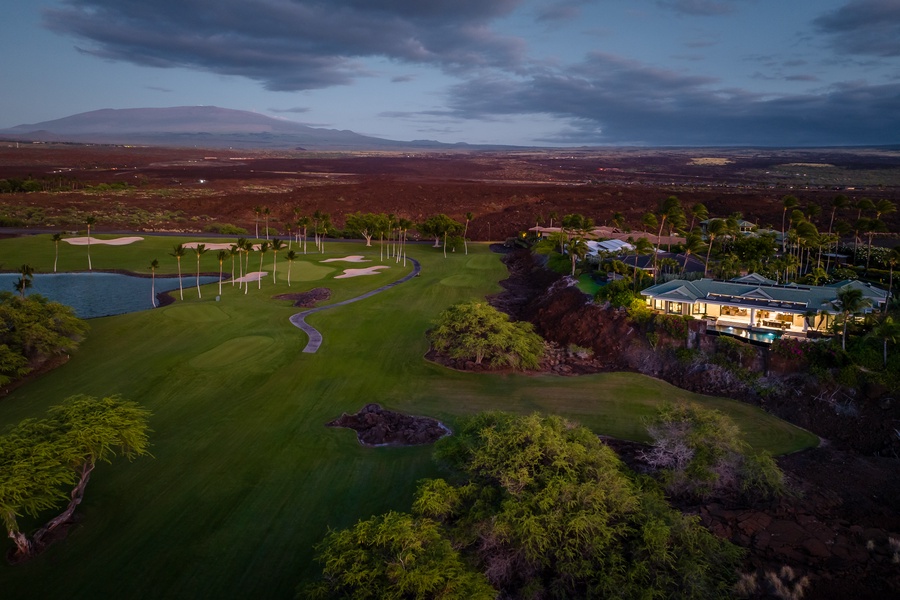 Aerial view of a scenic golf course at dusk, with lush greenery and a luxurious home.