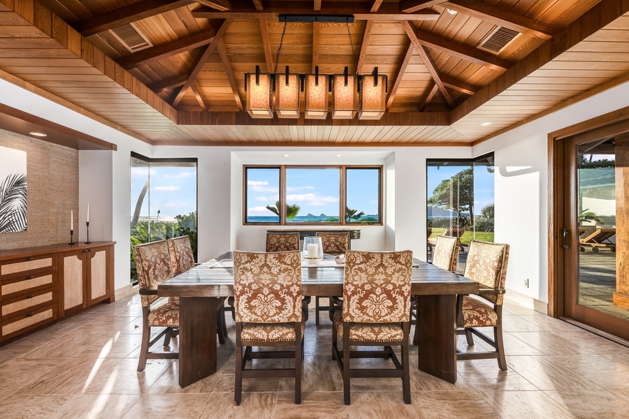 Indoor dining under a striking wood-beam ceiling with lush garden and ocean views.