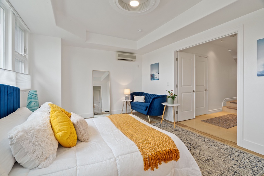 Experience the cozy ambiance of the primary suite, dominated by a plush white king bed topped with a striking yellow cushion and a complementary tasseled throw blanket.
