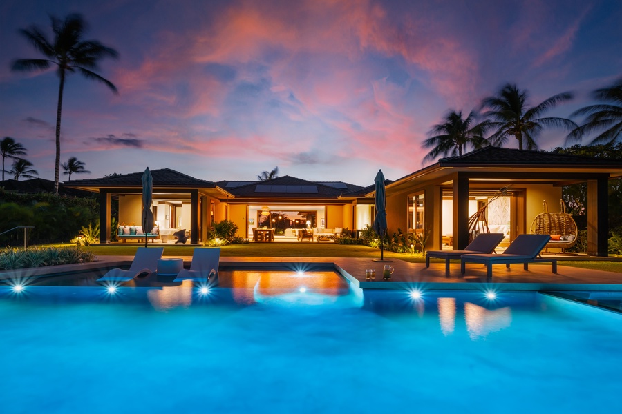 Picture-perfect tropical estate with illuminated pool reflecting dramatic sunset skies and swaying palm trees.