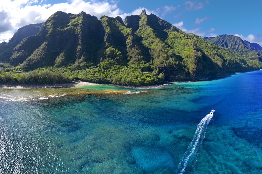 Ke’e Beach with vibrant blue waters and a boat navigating near the scenic Na Pali Coastline.