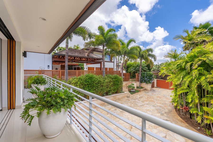 A quiet outdoor terrace overlooks tropical palms, lush gardens, and neighboring property structures under sunny skies with scattered clouds. Perfect for relaxing outdoors during your stay.