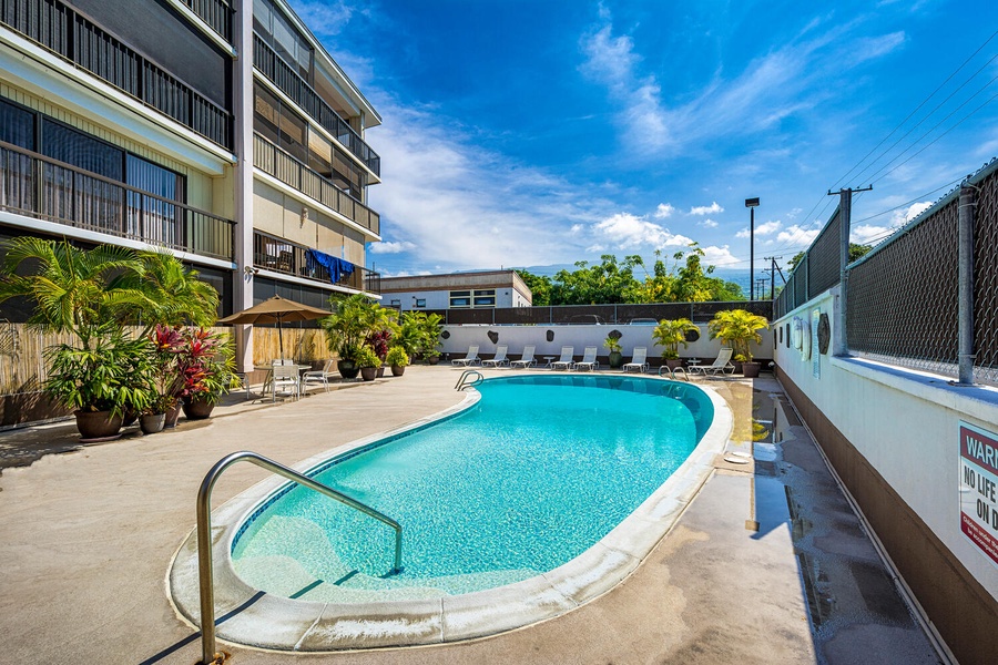 Refreshing pool area surrounded by tropical plants and comfortable lounge chairs under bright blue skies.