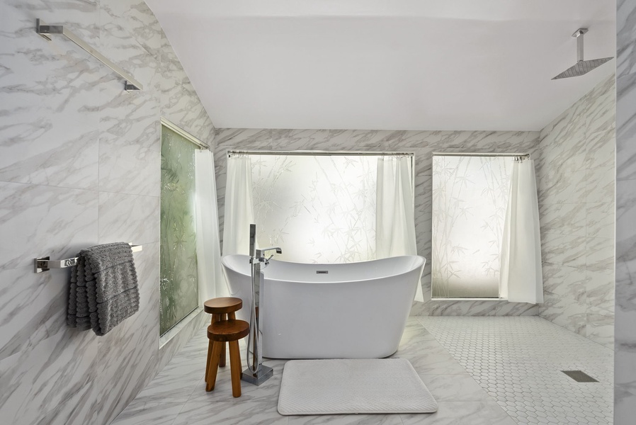 Soaking tub and rainfall shower set within a bright marble-lined sanctuary.