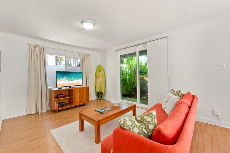 Your bright living space features comfortable seating, entertainment setup, and sliding glass doors opening to a tropical garden view—perfect for unwinding after beach adventures.
