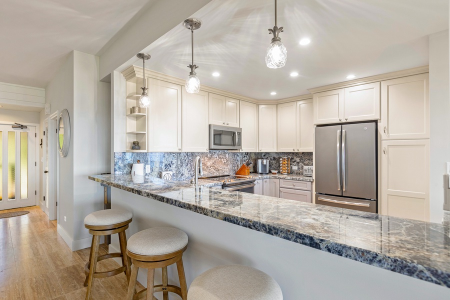 This spacious kitchen boasts elegant granite countertops and a breakfast bar with seating for three, illuminated by stylish pendant lighting.