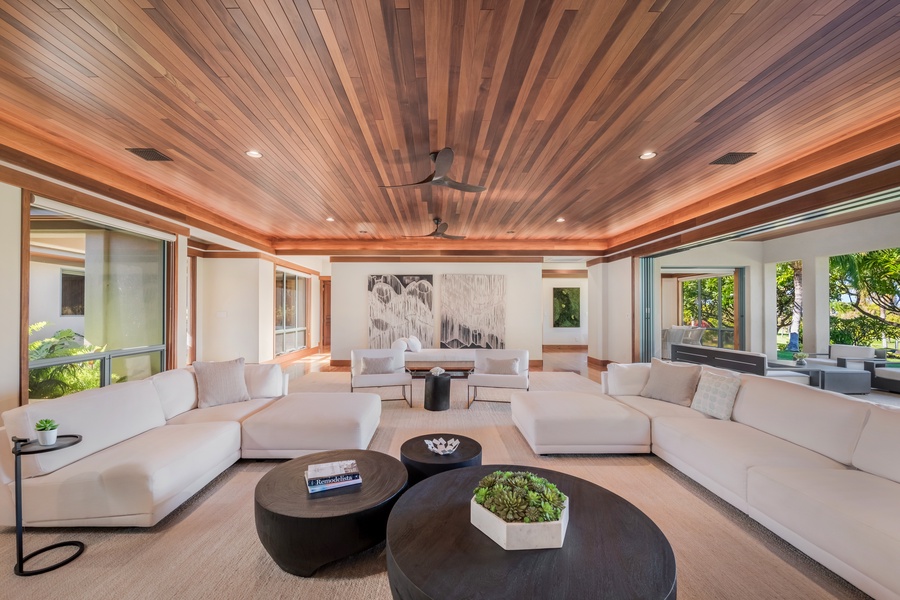 Spacious living room with luxurious seating, featuring a stunning wood-paneled ceiling and views of the lush outdoors.