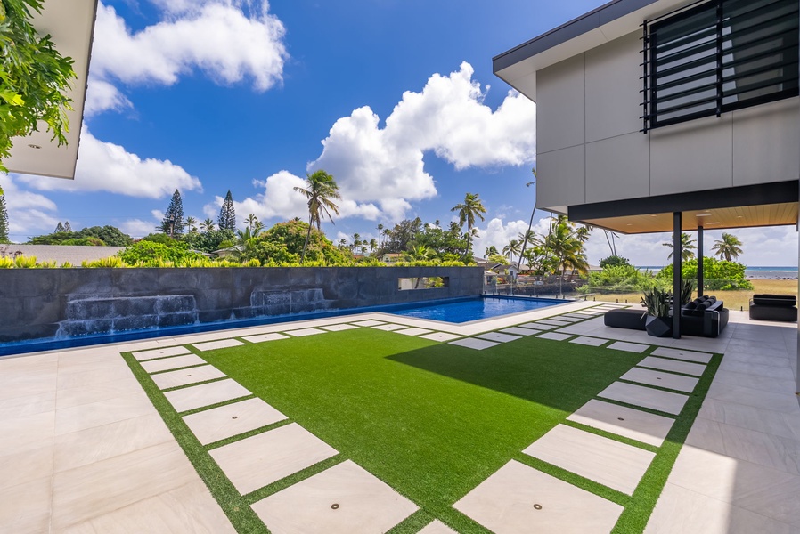 Manicured lawn and pool area set against swaying palms and open sky.