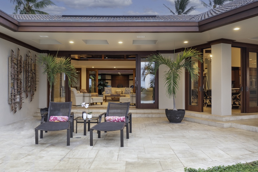 Elegant covered terrace seamlessly connects indoor luxury with tropical outdoor living through sophisticated design and lush palm accents.