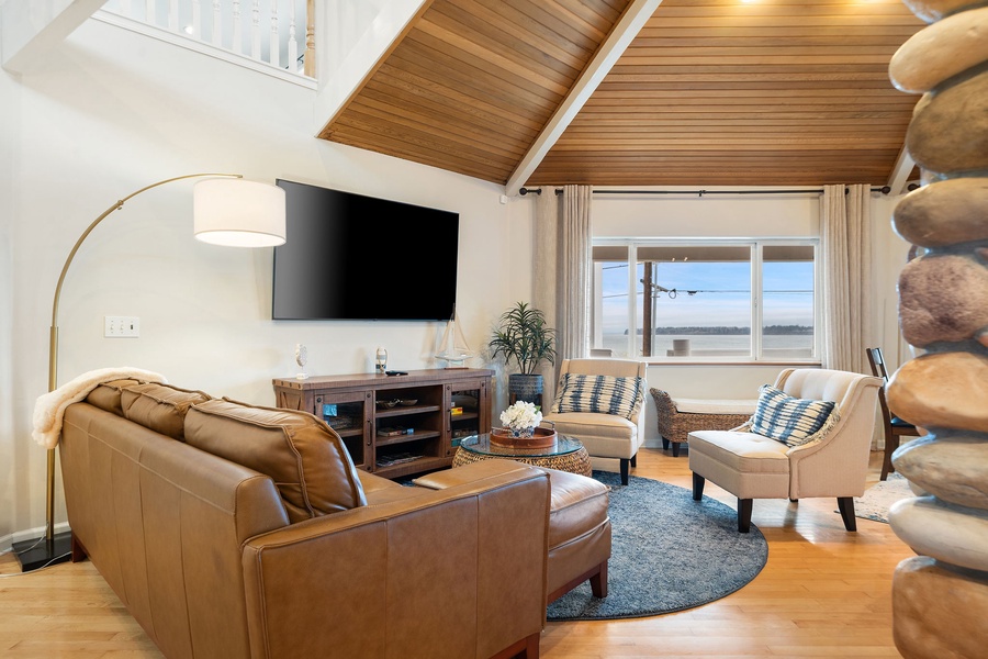Relax in your stylish living room with vaulted wood ceilings, leather sofa, and peaceful water views through large windows.