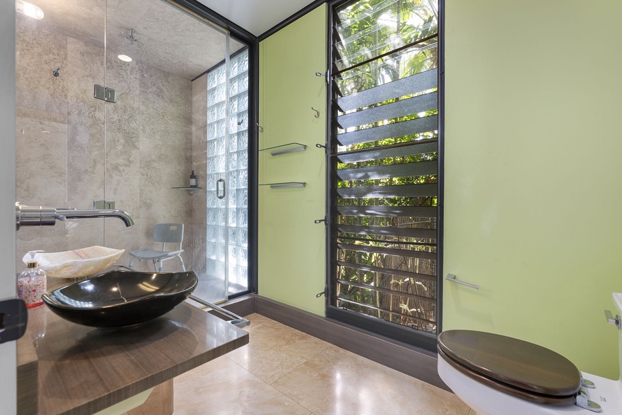 A spa-like ensuite with a glass shower, modern sink, and lush greenery views.