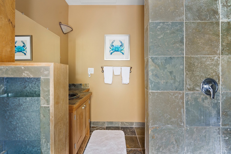 Unwind in your private spa-like bathroom featuring beautiful stone tile work, coastal crab artwork, and fluffy towels waiting for your arrival.