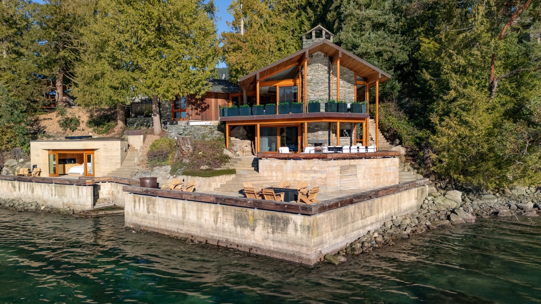 Stunning lakefront property featuring contemporary architecture with stone and wood elements, surrounded by pristine natural landscape and crystal-clear waters.