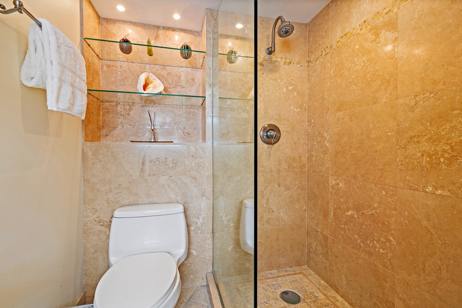 The bathroom at Royal Kahana 610 offers a walk-in shower with sleek glass doors and built-in shelving.