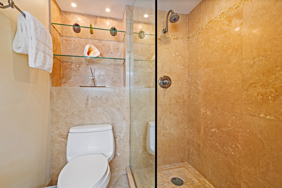 The bathroom offers a walk-in shower with sleek glass doors and built-in shelving