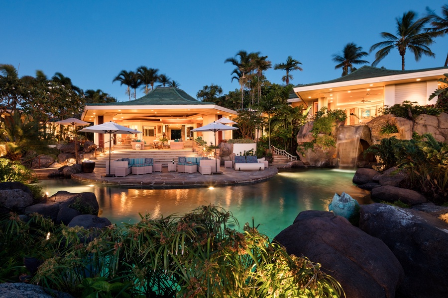 Twilight view of estate home with pool, pool deck, lanai, great room, and primary suite (on right).