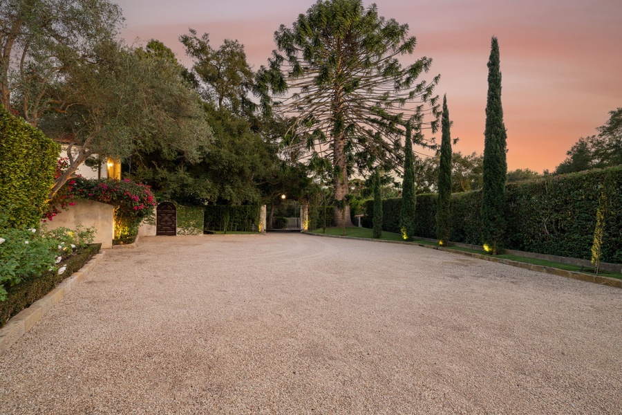 A romantic sunset paints the sky as the property's entrance welcomes guests with landscaped gardens and ample parking space.
