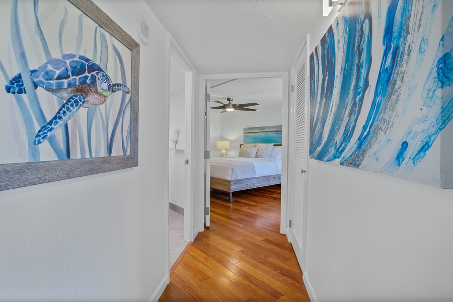 A bright hallway leads to the inviting bedroom, featuring warm wood floors and calming artwork.