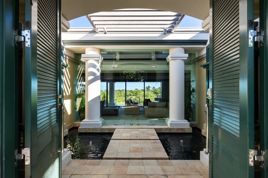 Elegant entryway with towering columns and water features, leading to an inviting indoor space.