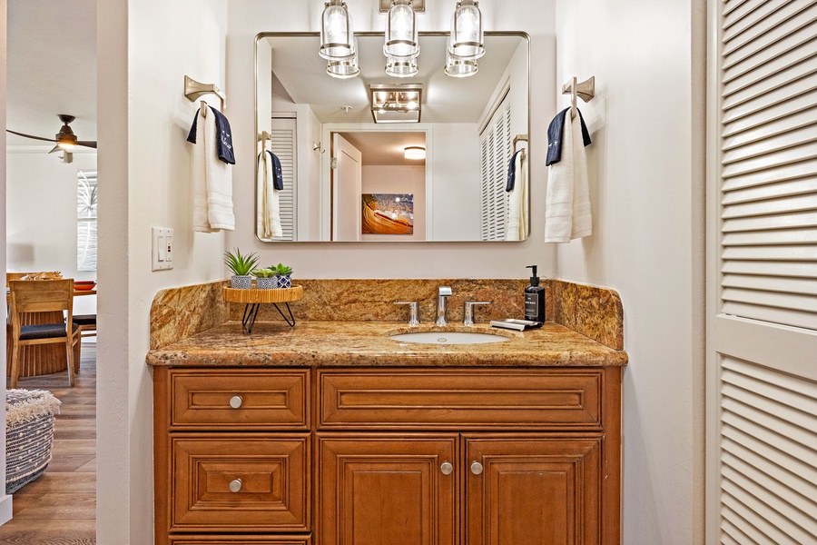The bathroom at Mahana 1118 boasts granite counters, rich wood cabinetry, and modern fixtures.