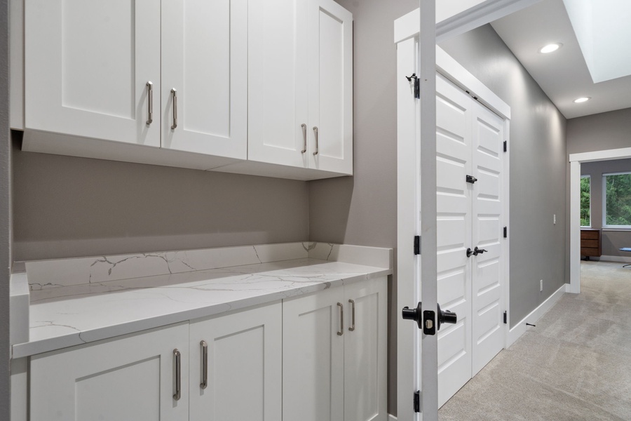 Your bright laundry room features crisp white cabinetry and marble-look countertops for easy organization.