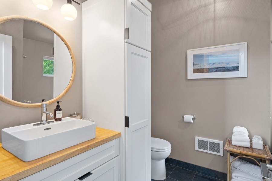 Modern ensuite with a round mirror, wood vanity, and soft lighting.