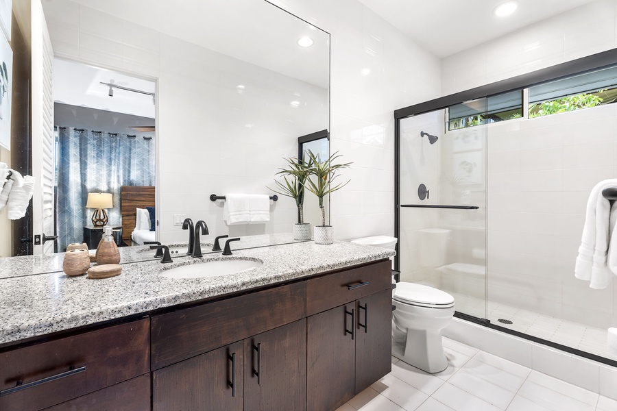Pamper yourself in this modern bathroom featuring granite countertops, elegant dark cabinetry, and a pristine walk-in shower with glass doors.