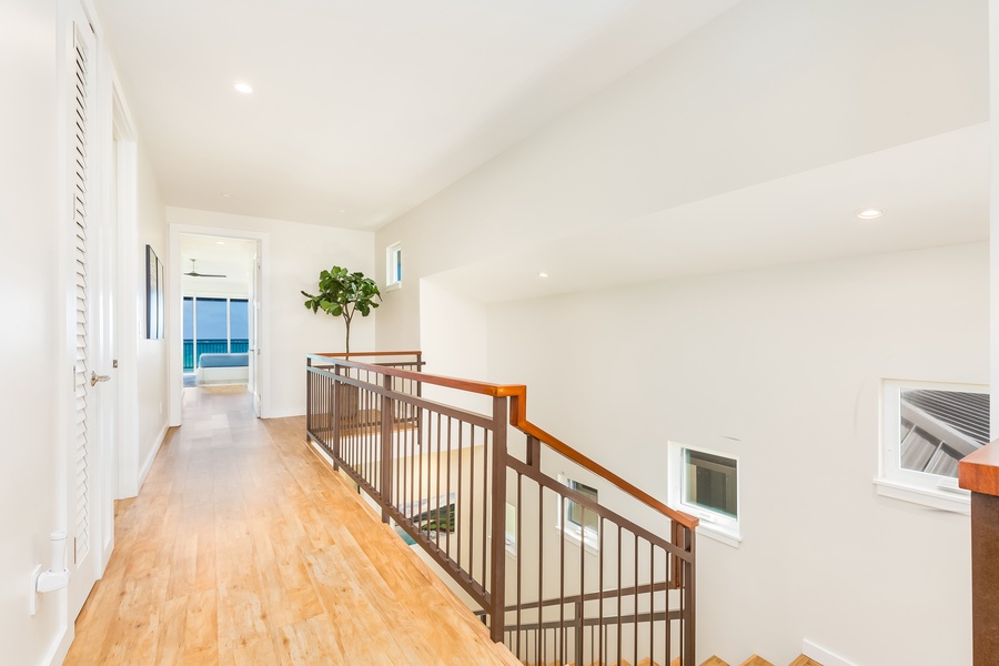 Hallway with wood flooring, white walls, and large windows creating a bright, open space.