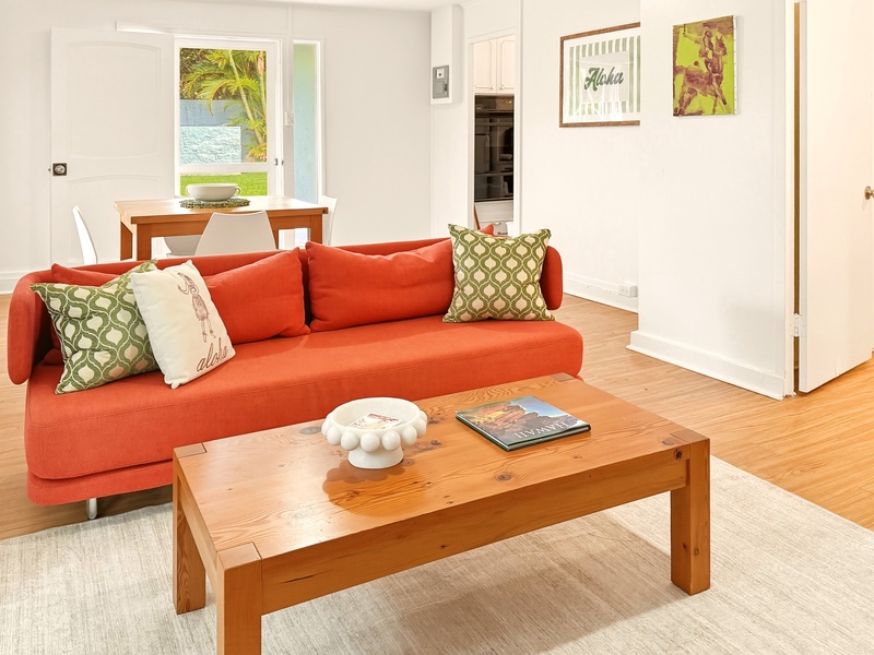 Settle into this vibrant open-plan living space where warm wood floors and cheerful orange seating create your perfect relaxation zone.