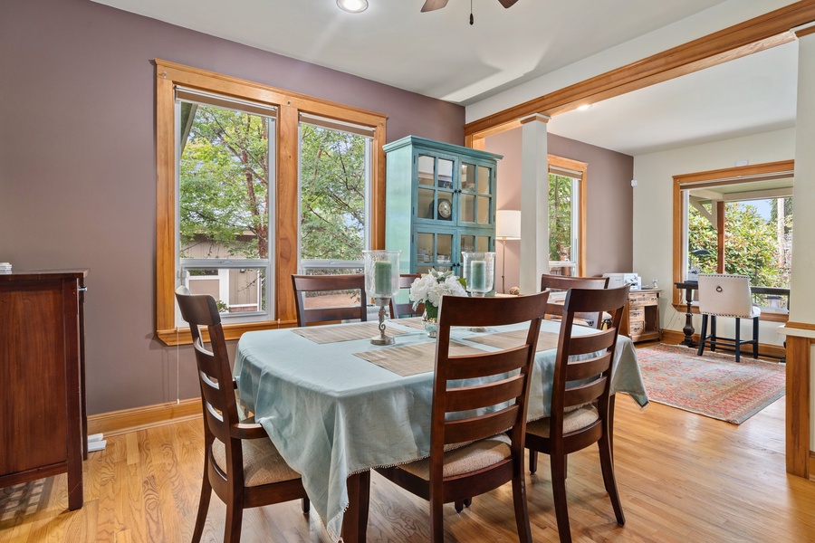 Your elegant dining space features rich wood details and floods with natural light through expansive windows overlooking leafy trees.