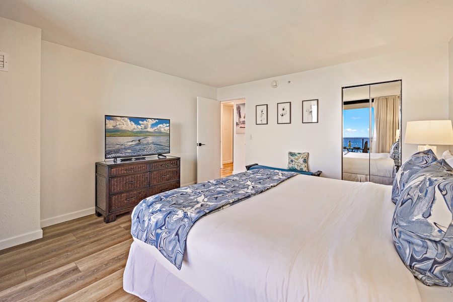 The bedroom offers a serene retreat with a comfortable bed, flat-screen TV, and a view of the ocean just beyond the sliding glass doors.