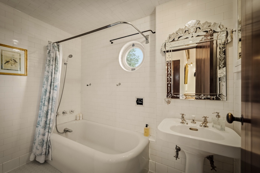Your elegant bathroom features a deep soaking tub, vintage-style fixtures, and charming round porthole window for natural light.