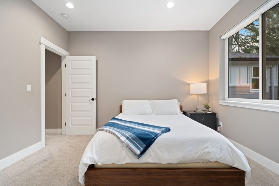 Sink into crisp white linens and soft carpeting in your peaceful bedroom retreat, where natural light and modern comfort create the perfect rest.
