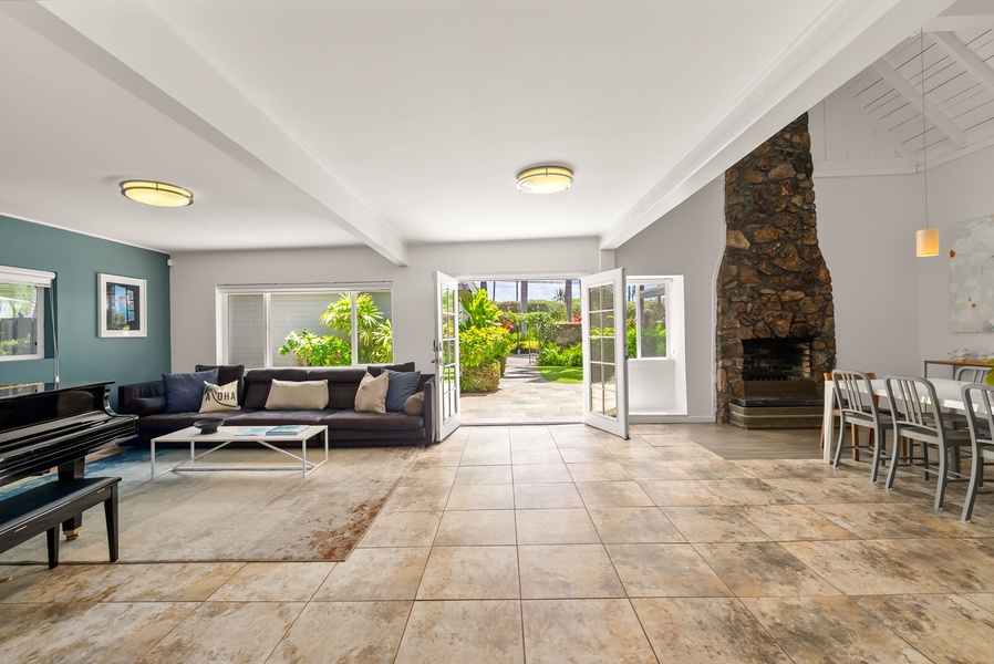 Step into your sunlit sanctuary where modern comfort meets natural beauty. French doors frame lush garden views, inviting the outdoors in as you unwind by the striking stone fireplace.