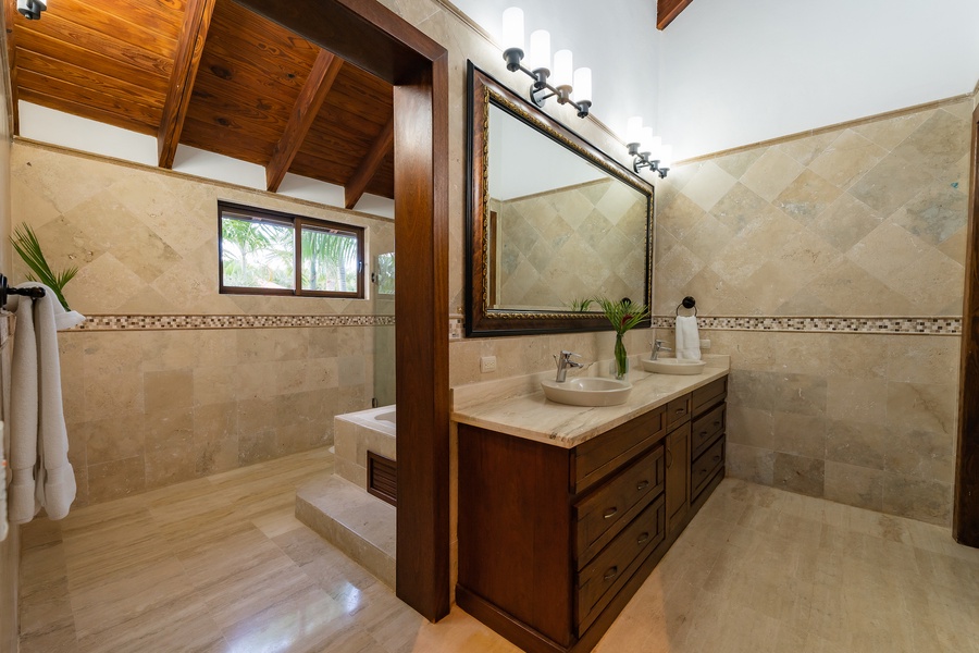 Luxurious ensuite bathroom with natural stone finishes and a large mirror.