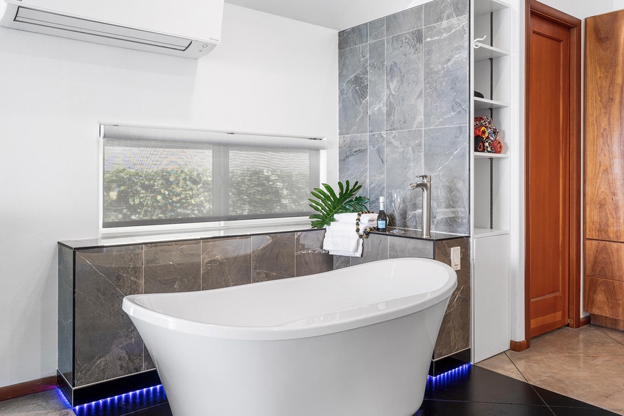 Luxury bath with soaking tub, spa lighting, and window views of lush greenery.