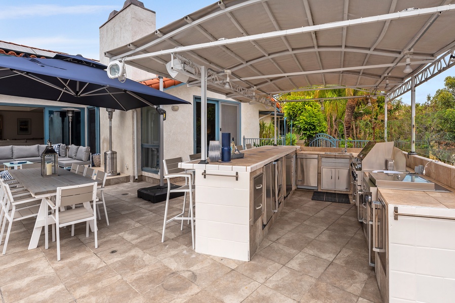 A BBQ chef's dream kitchen with outdoor wok, professional grade BBQ, double burners, sink, wine cooler, ice maker, refrigerator and an outdoor shower on the other side.