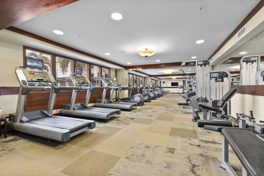 Your well-equipped fitness center features modern cardio and strength equipment with natural light streaming through elegant wooden blinds.