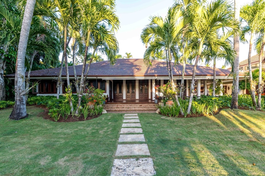 A welcoming front porch surrounded by lush greenery and towering palm trees.