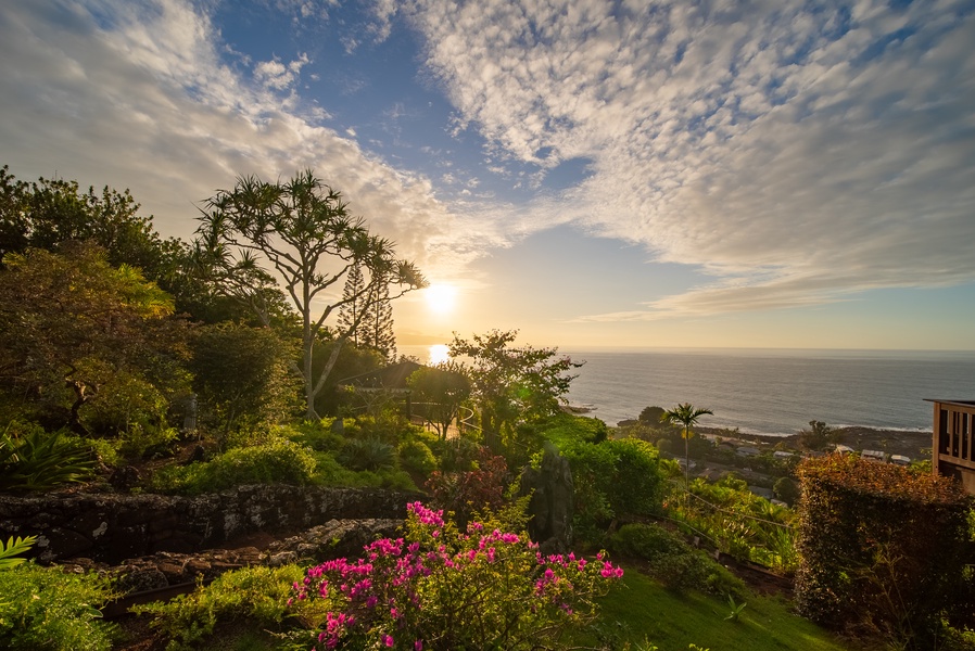 Stunning coastal sunset illuminates lush tropical gardens overlooking the ocean, creating a breathtaking natural backdrop for the property.