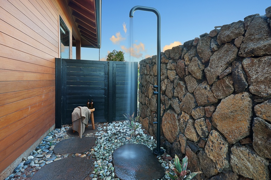 Private outdoor shower surrounded by lava rock and tropical greenery.
