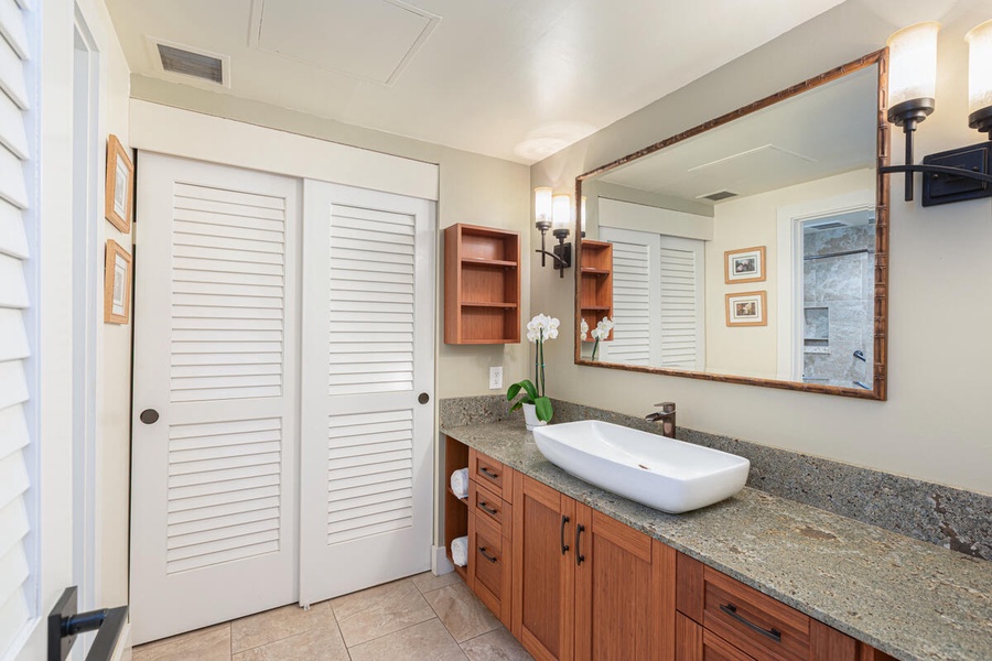 Primary bath with large mirror, vessel sink, and wood cabinetry.