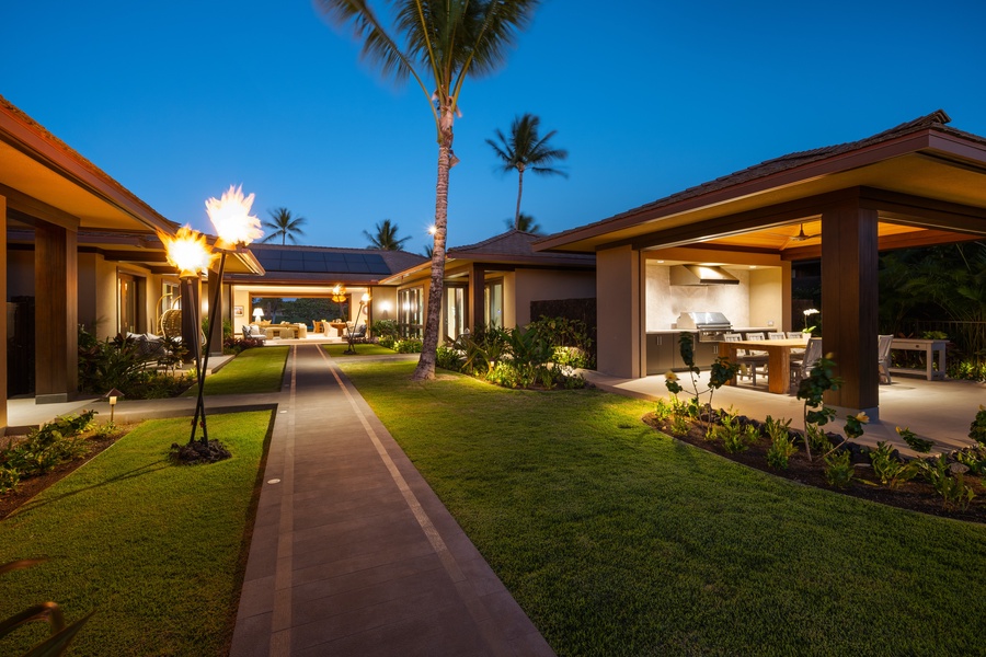 Tropical luxury estate with manicured gardens, palm trees, and elegant outdoor living spaces illuminated under the evening sky.