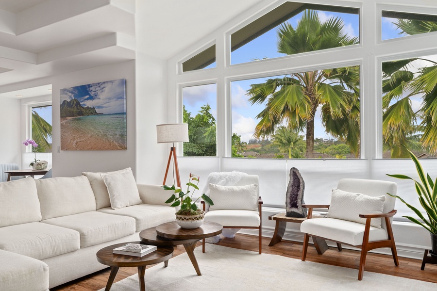 Relax in a serene living area with floor-to-ceiling windows offering a panoramic view of lush palms, complemented by chic decor and inviting white couches for your stay.